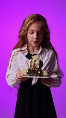 Doğum günü pastasında mum söndüren 8 yaşında tatlı bir kız. Ellerinde pasta tutan neşeli bir kız. Tatlı çocuğun doğum günü.