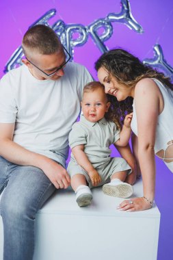 Genç anne ve baba beyaz arka planda bir yaşındaki oğullarıyla oynuyorlar. Küçük çocuk ve anne ve baba gülüşüyorlar. Mutlu anne ve çocuklu baba..