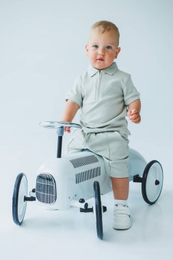 Sevimli ve neşeli bir çocuk büyüleyici bir eski model oyuncak arabada güven içinde poz veriyor. Parlak ve neşeli bir stüdyoda saf mutluluğun özünü yakalıyor.