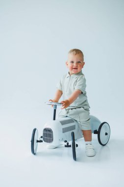 Şortu ve tişörtü olan takım elbiseli şık bir çocuk araba sürüyor. Beyaz arka planda oyuncak arabalı küçük bir çocuk..
