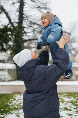 Gülümseyen anne bir yaşındaki oğluyla sokakta oynuyor. Çocuk gelişimi ve aktif eğlence. Küçük çocuk annesiyle oyun parkında oynuyor..