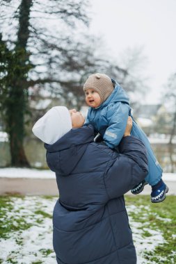 Gülümseyen anne bir yaşındaki oğluyla sokakta oynuyor. Çocuk gelişimi ve aktif eğlence. Küçük çocuk annesiyle oyun parkında oynuyor..