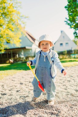 Küçük çocuk oyun parkındaki kum havuzunda kürekle oynuyor. Doğada oynayan bir çocuk. 2 yaşındaki bir çocuk güneşli bir yaz gününde parkta yeşil çimlerin tadını çıkarıyor..
