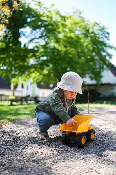 Küçük çocuk dışarıda plastik arabasıyla oyun parkında oynuyor. Bahçede arabasıyla oynayan 2 yaşında tatlı bir çocuk. Çocuk dışarıda yürüyor..