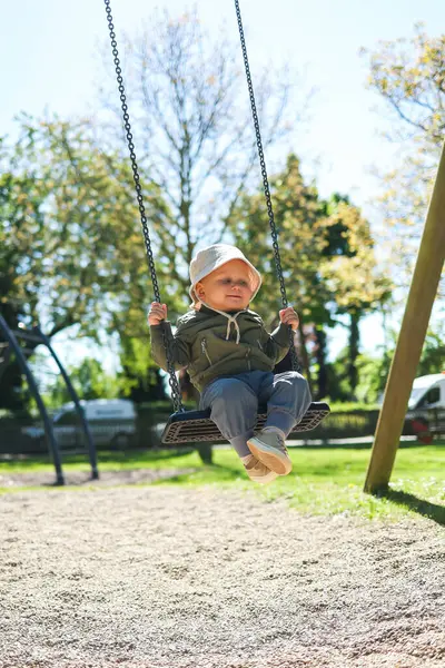Kafasında Panama şapkası ve salıncakta sallanan açık renk ceketli sevimli 2 yaşında bir çocuk. Parktaki bir çocuk parkında salıncak. Bebek salıncakta sallanıyor. Şık çocuk kıyafetleri..