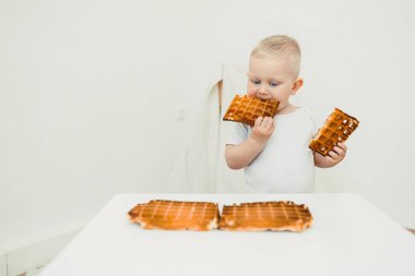 Neşeli bir çocuk, mutlu bir şekilde lezzetli waffle 'ların tadını çıkarıyor. Hisleri harekete geçiren parlak, canlı renklerle süslenmiş minimalist bir ortamda sevimli ve eğlenceli bir sahne yaratıyor.