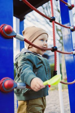 Renkli şapkalı neşeli bir çocuk, sonbahar renkleriyle çevrili bir oyun parkına tırmanıyor. Anıları keşfederken ve yaratırken mutluluk saçıyor.