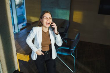 Bir kadın cep telefonuyla konuşurken neşeyle gülüyor, sohbetinin tadını çıkarıyor ve mutlu hissediyor.
