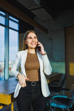 Beyaz ceketli bir kadın aktif olarak cep telefonuyla konuşuyor. Önemli bir sohbete katılmış gibi görünüyor.