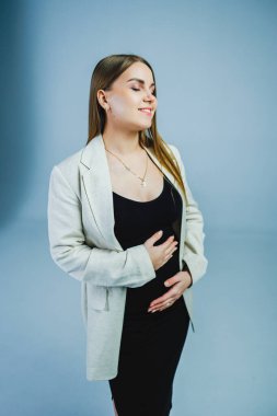 Şık beyaz bir ceketle şık siyah bir elbise giyen bir kadın zarif bir şekilde elini göğsüne dayar ve zarafet saçar.
