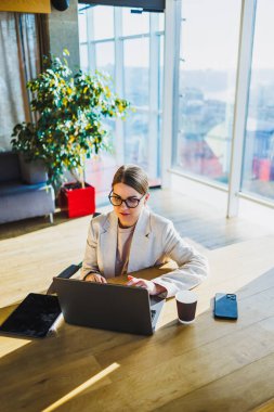 Parlak, modern bir ofis alanında resmi giyinmiş kararlı bir kadın özenle dizüstü bilgisayarı üzerinde çalışıyor. Etrafında oldukça verimli bir atmosfer yaratıyor.