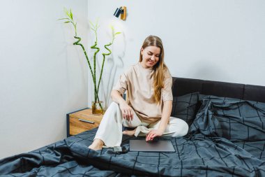 Sakin genç bir kadın, minimalist bir yatak odasında sakin bir şekilde dinleniyor. Canlı bitkilerle dolu. Huzur ve konfor sağlayan sakin bir atmosfer yaratıyor.