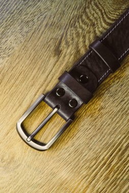 Bu kaliteli kahverengi deri kemer şık bir metal toka ile eşleştirildiği her kıyafeti güzelleştirir. Zarif bir şekilde ahşap yüzeyde sergileniyor.