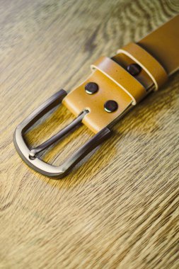 Parlak metal tokalı bu şık kahverengi deri kemer moda tutkunları için mükemmeldir. Zengin, ahşap bir arka planla güzel bir tezat oluşturur.