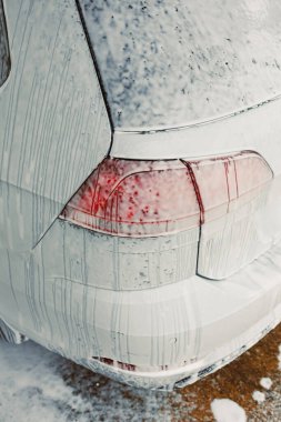 Arabanın arka tarafındaki bu yakın plan yıkama sırasında köpükle kaplandığını gösteriyor. Yüzeyinde sabun köpükleri ve parlak kırmızı stop lambaları, temizlik sürecinin altını çiziyor.