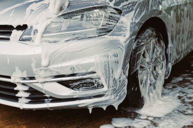 Kalın köpük ve sabun köpüğüyle kaplanmış pırıl pırıl gümüş bir arabanın yakın çekimi. Bu resim araba bakımı ve detaylarının önemini vurgular