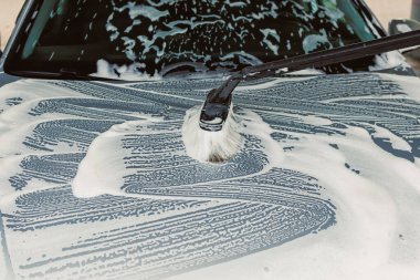 Bu resim yoğun köpüklü sabunlarla kaplı bir kaput tasvir ediyor. Silecek bıçağı, genel araba yıkama işlemi sırasında suyu aktifleştirmekle meşgul.