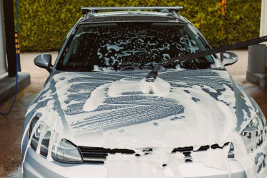 Otomobil yıkama istasyonunda köpükle temizlenen bir arabanın yakın çekim görüntüsü. Etkili araba temizleme teknikleri sergiliyor.