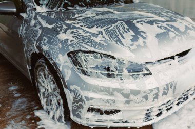 Profesyonel bir temizlik servisinde köpükle yıkanan parlak gümüş renkli bir araba, uzun yaşam ve estetik cazibe için düzenli bakım ihtiyacını vurguluyor