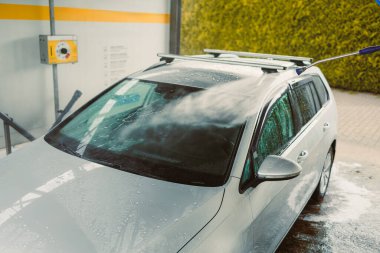 Parlak gümüş renkli bir araba su ile yıkanmakta. Bencilce hizmet veren bir araba yıkama tesisinde, kabarcıklar ve kalın köpükler yüzeyinde belirgin bir şekilde görülüyor.