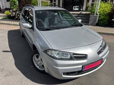 Zarif, gümüş renkli bir araba arka planda canlı bir bahçesi olan güzel bir caddede park halinde. Otomotiv vitrinleri ve reklamlar için ideal.