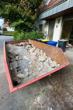 Sakin bir sokakta taşan bir enkaz yığını, devam eden ev yenilemelerini gösteriyor ve projelerin yenilenmesi konusunda mahallelerin atık yönetimi uygulamalarını yansıtıyor