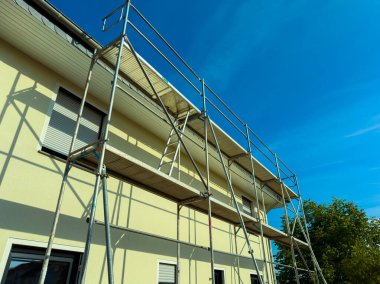 Bu resim iyi inşa edilmiş bir yapı gösteriyor, bina bakımı sırasında işçilerin güvenliğini sağlıyor, parlak mavi gökyüzüne karşı, güvenliği ve ulaşılabilirliği vurguluyor.