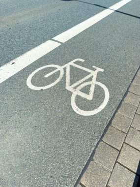 Büyük ve belirgin bir beyaz bisiklet şeridi sembolü açıkça görülüyor, dokulu bir asfalt yüzeye boyanmış, kentsel alanlarda herkes için güvenliği ve bisiklet sürmeyi teşvik eden bir resim.