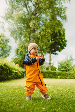 Parlak turuncu yağmurluk giymiş neşeli bir çocuk güzel çiçeklerden oluşan renkli bir bahçeyi keşfeder. Saf neşe ve merakla dolu unutulmaz anlar yaratır.