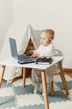 Renkli dekorlar ve fayanslarla çevrili şık bir oyun masasında dizüstü bilgisayarda kısa saçlı bir çocuk yaratıcılık için parlak bir atmosfer yaratıyor.