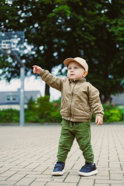 Şık ceketli ve şirin şapkalı enerjik bir bebek dışarıda gezer, çeşitli şeylere işaret eder, saf merakı ve çocukluk keşfinin ruhunu somutlaştırır.