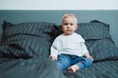 Çekici bir bebek, yumuşak yastıklarla çevrili, rahat bir yatakta oturur, sıcak kapalı bir alanda merak ve masumiyet gösterir, neşeli anları yakalamak için idealdir.