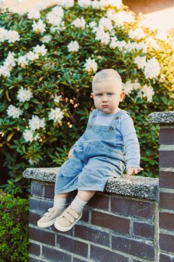 Tulum giymiş genç bir çocuk, çiçek açan, neşe ve masumiyeti temsil eden, aile veya çocukluk temalarını gösteren canlı bir çiçek zeminine karşı samimi bir anda yakalanır.