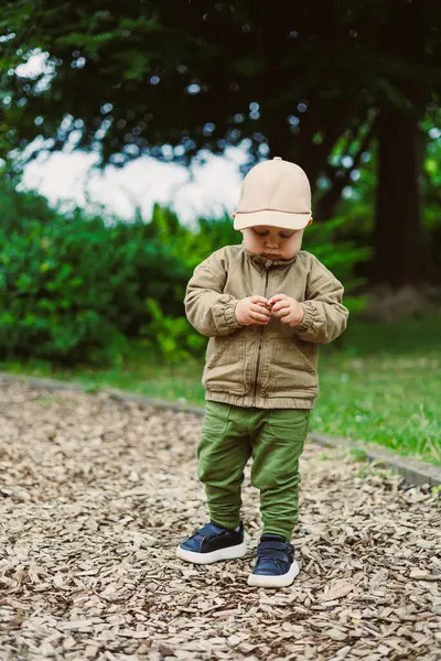 Neşeli ve neşeli bir çocuk oyun sahasında eğlenceli aktivitelere katılır. Zeytin yeşili bir elbise ve doğası gereği güzelliklerle çevrili şirin bir bej şapka giyer.