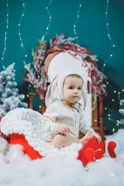 Tavşan kostümü giymiş 1 yaşında bir çocuk Noel ağacının yanında oturuyor. Çocuklar için yeni yıl kutlaması