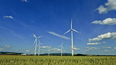 Buğday tarlalarıyla çevrili, sürdürülebilir enerji ve doğal güzelliği sembolize eden parlak mavi gökyüzüne karşı bir rüzgar türbini dimdik ayakta duruyor. Avrupa 'da tarım alanlarında rüzgar türbini güç üretimi