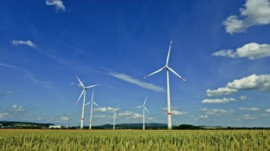 Buğday tarlalarıyla çevrili, sürdürülebilir enerji ve doğal güzelliği sembolize eden parlak mavi gökyüzüne karşı bir rüzgar türbini dimdik ayakta duruyor. Avrupa 'da tarım alanlarında rüzgar türbini güç üretimi