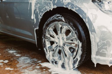 Parlak gümüş bir sedan titizlikle yıkanırken, köpük köpükleri tekerlekleri kaplıyor, her yerde gururlu sahiplerinin hayran olduğu olağanüstü araba bakımını sergiliyor.