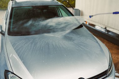 Hareketli bir oto yıkamada, yüksek basınçlı su spreyi parlak gümüş bir arabayı etkili bir şekilde temizler, gelişmiş araba bakım teknikleri ve detaylara titizlikle dikkat eder.