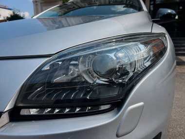 Modern gümüş renkli bir arabanın büyüleyici yakın çekimi, parlak kıvrımlarını, karmaşık ayrıntılarını ve gelişmiş otomotiv tasarımını gözler önüne seren yansımalarını vurguluyor.