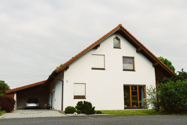 Bu modern beyaz ev eşsiz eğimli bir çatıya sahiptir ve yemyeşil ile çevrilidir. Geniş garaj yolu, uzun bir günün ardından dinlenmek için sakin bir ortam sunuyor.