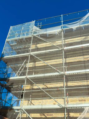 Bu göz alıcı görüntü, inşaat ve mimariyle ilgili temalar için ideal olan canlı mavi gökyüzüne karşı güvenlik özellikleri taşıyan inşaat iskelesini gözler önüne seriyor