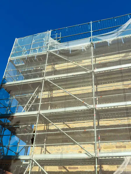 Bu göz alıcı görüntü, inşaat ve mimariyle ilgili temalar için ideal olan canlı mavi gökyüzüne karşı güvenlik özellikleri taşıyan inşaat iskelesini gözler önüne seriyor