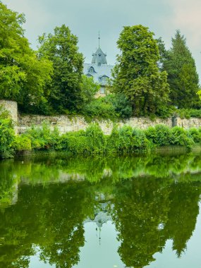 Çarpıcı tarihi bir bina, yemyeşil yemyeşil sularla çevrili huzurlu nehir sularına güzel bir şekilde yansıyor, doğal güzelliğin değerini ve sükunetini çağrıştırıyor.