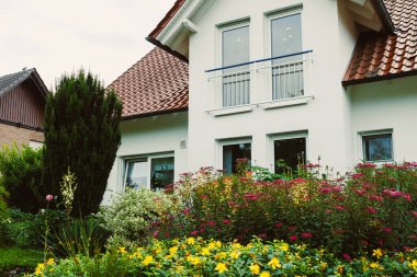 Canlı bir çiçek bahçesinin yanındaki bu çarpıcı beyaz ev, her güzel ev için yaratıcı peyzaj fikirlerine ilham veren zarif mimari özellikler sergiliyor.