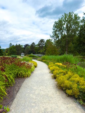 Canlı çiçekler ve yemyeşil çiçeklerle bezenmiş sakin bir bahçe yolu keşfedin, sakin yürüyüşler için ideal bir atmosfer yaratın ve doğal güzelliğin tadını çıkarın.