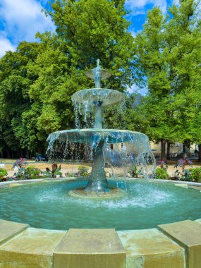 Çok güzel tasarlanmış, çağlayan sularla dolu çok katmanlı bir çeşme yeşillik ve çiçeklerle dolu canlı bir parkta oturuyor. Rahatlamak ve doğanın tadını çıkarmak için ideal.