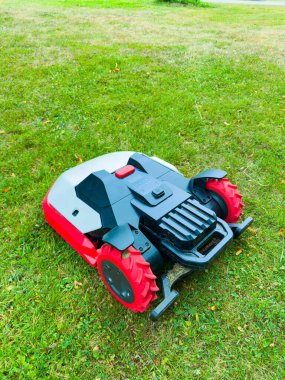 Şık, modern bir robotik çim biçme makinesi sağlam bir tasarımı ve parlak kırmızı röfleleri olan yemyeşil çimlerin üzerinde zarif bir şekilde duruyor, keskin kenarlı peyzaj teknolojisi sergiliyor.