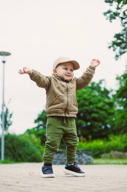Neşeli bir çocuk kolları açık, doğayı kucaklayan bir şekilde dışarıda duruyor. Samimi bir kıyafet giyip, canlı bitkilerle dolu yemyeşil bir ortamda mutluluk yayıyorlar.