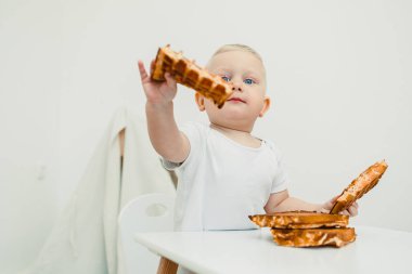 Neşeli bir bebek, altın bir waffle 'a ulaşmaya hevesle uzanır, keyifli bir aile anını yakalar, birlikte geçirdiğimiz eğlenceli deneyimleri ve uzun süreli anıları vurgular.